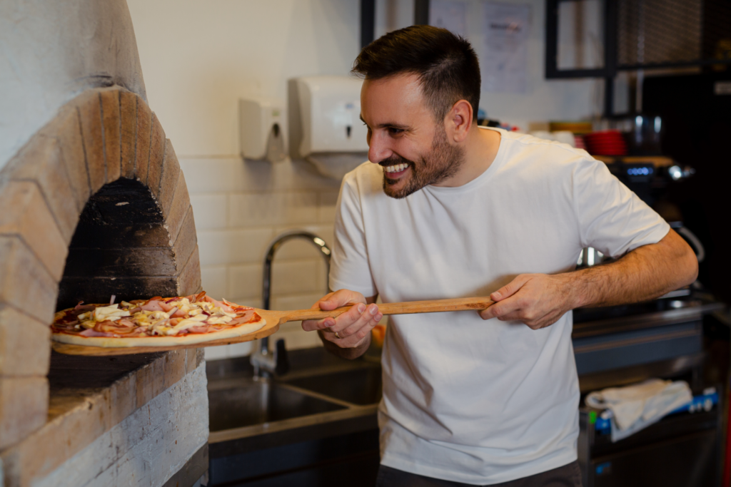 A pizza chef inserts a pizza into a brick oven.
