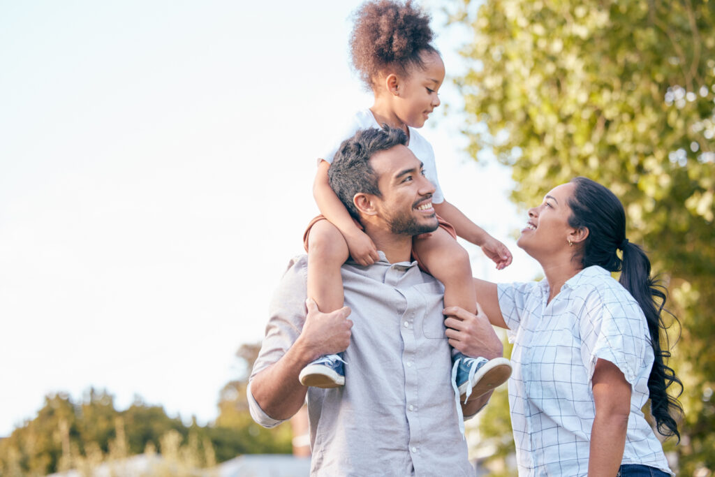Mother, Father, and Daughter smiiling in a park.